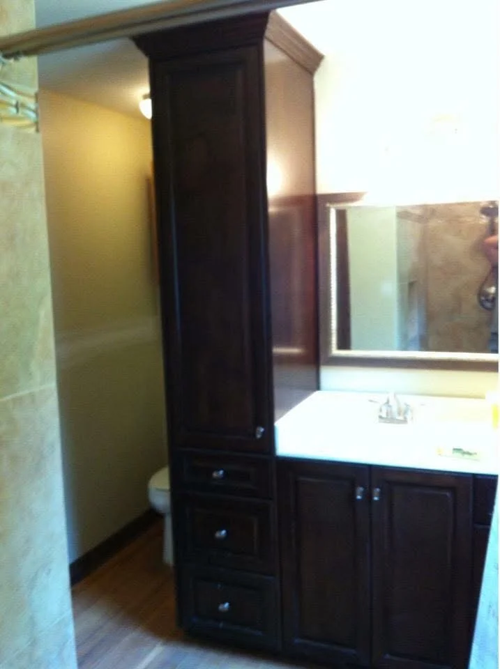 Dark wood bathroom vanity with tall storage tower, white countertop, and framed mirror