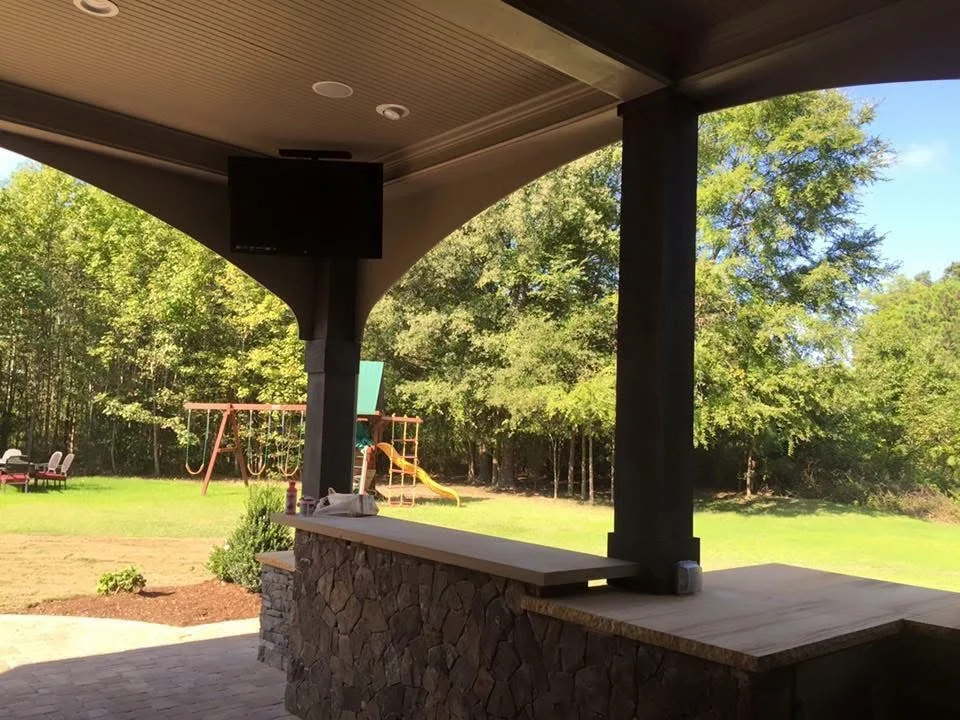 Covered patio with stone base, black columns, coffered ceiling, and recessed lighting overlooking lawn