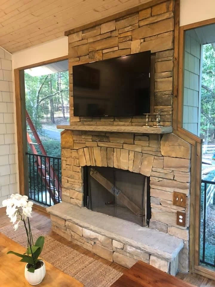 Stacked stone fireplace with mounted TV, wooden mantel, and metal firebox surround