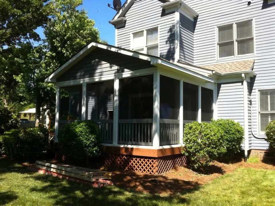 Screened porch with white frame, full windows, pitched roof, and brick lattice foundation on colonial home