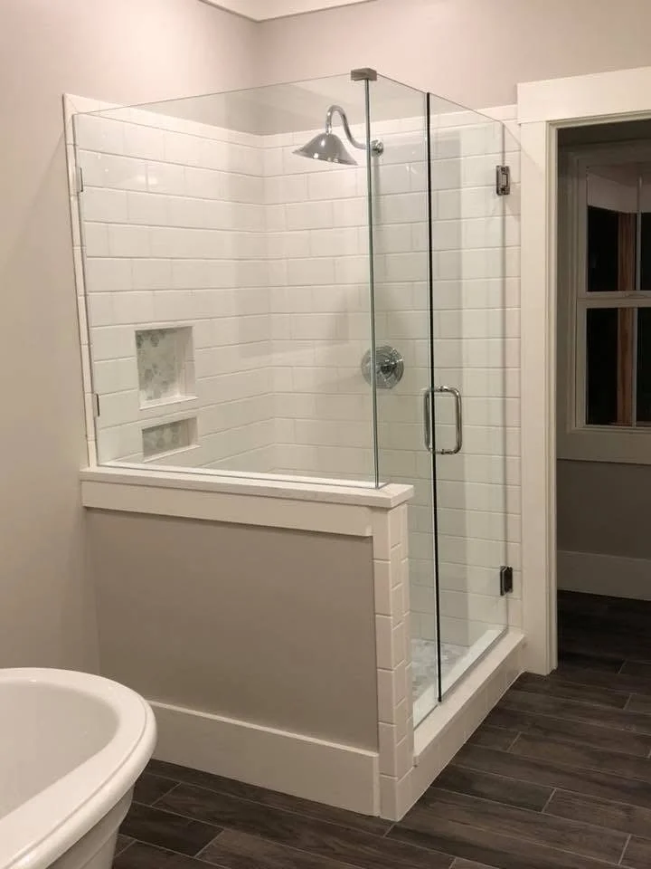 Frameless glass shower enclosure with chrome hardware, white subway tile walls, and integrated shelving niches