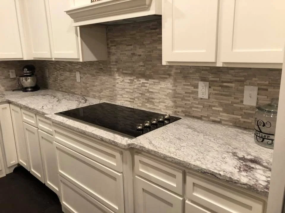 White kitchen cabinets with granite counters, stacked stone backsplash, and black cooktop island