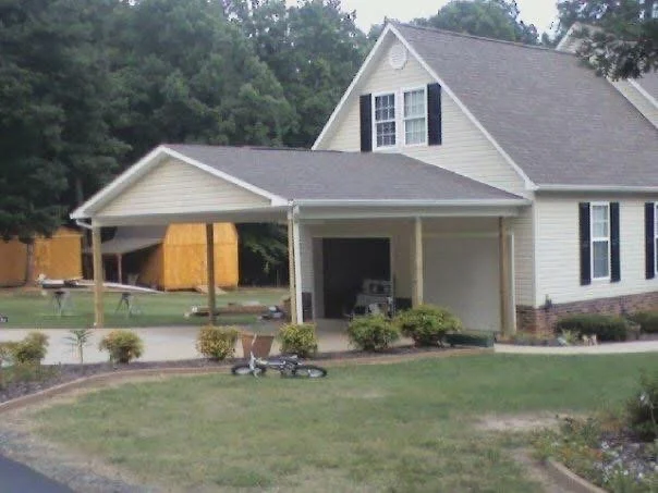 White covered porch addition with concrete pad, gable roof, and landscaping