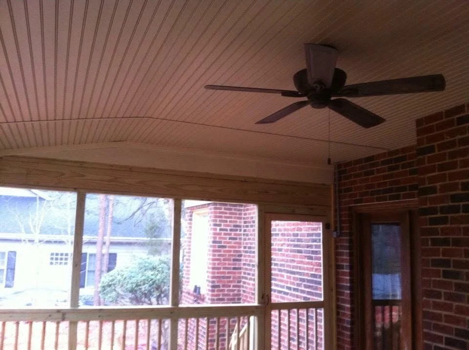 Screened porch with corrugated metal ceiling, wood beams, ceiling fan, and fixed windows