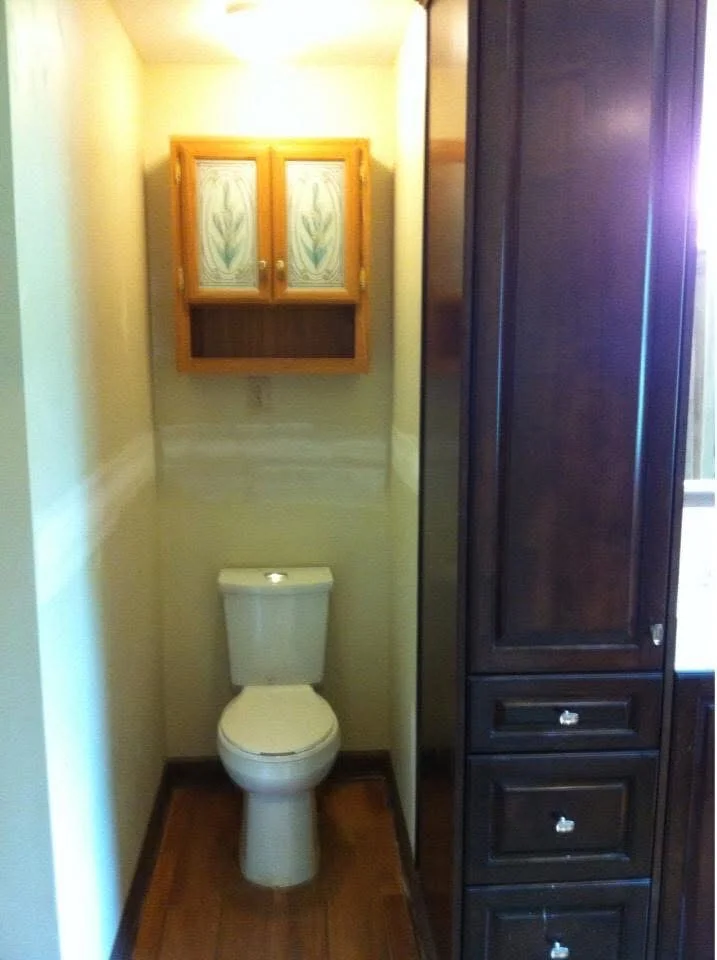Bathroom with yellow-green walls, hardwood floor, wood medicine cabinet with glass doors, and dark wood cabinetry