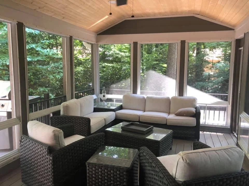 Screened sunroom with vaulted wood ceiling, multi-panel glass windows, wicker furniture, and composite deck