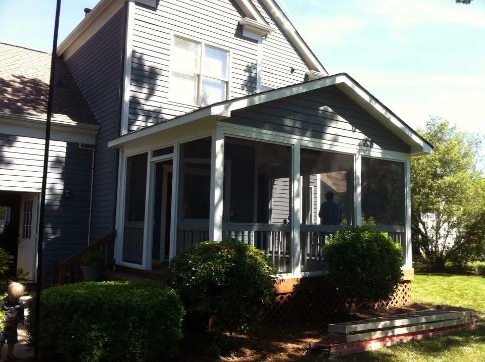 White screened porch addition with metal frame, screen panels, and wooden deck attached to vinyl-sided home