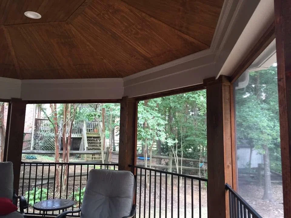 Screened porch with wood ceiling, metal railings, and full-height screen panels overlooking wooded area