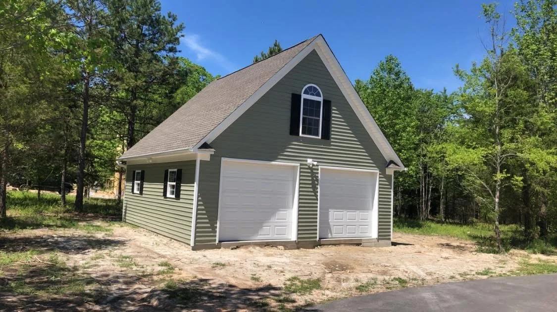 Two-car garage with gray siding, white doors, gable roof, and arched window
