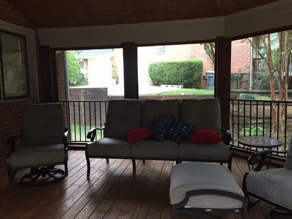 Screened porch with composite deck, black frame, and large windows overlooking brick home and landscaping