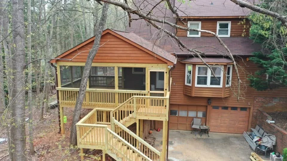 Pressure-treated wood screened porch with gable roof, railings, and attached deck stairs on wooded property