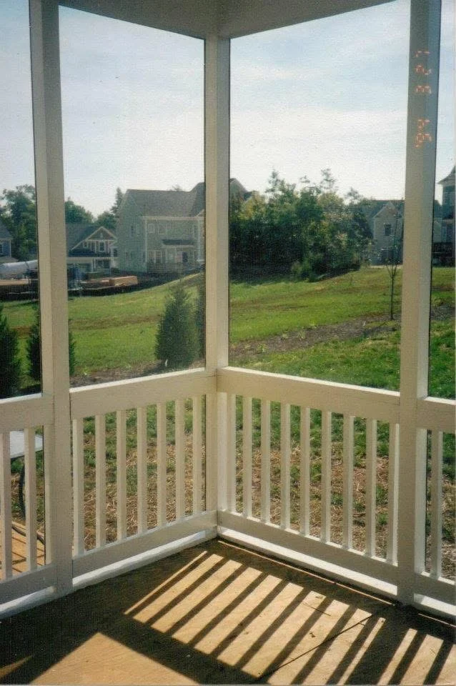 Screened porch interior with vinyl railings, glass panels, and wood flooring overlooking residential yard