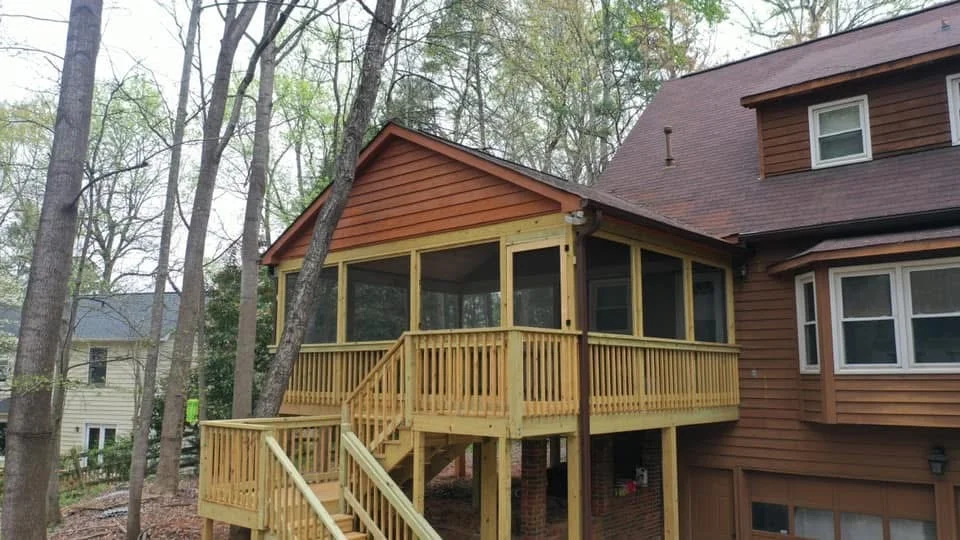 Cedar screened porch with large windows, wooden deck, and turned balusters attached to brick home