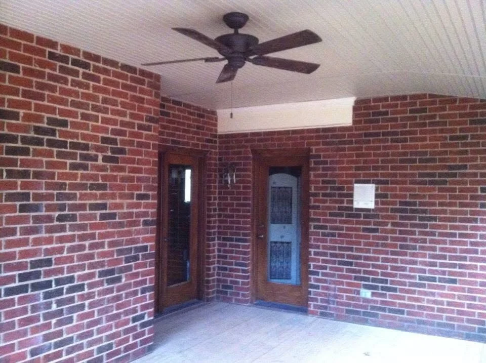 Brick interior room with white ceiling, ceiling fan, and wooden glass-panel doors