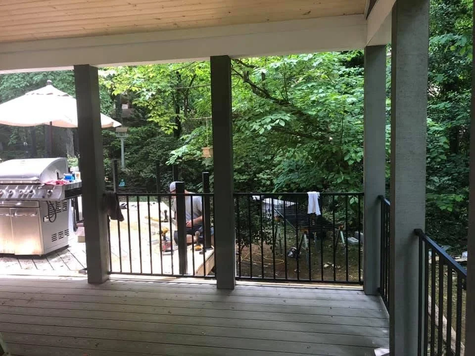 Composite deck with black metal railings, support posts, and multi-level design overlooking trees