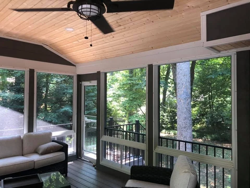 Screened porch with glass doors, wood vaulted ceiling, and metal railings overlooking forest